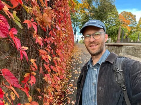 Man in Oslo next to a wall of fall colored leaves